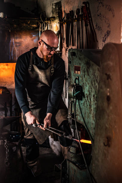 istock Blacksmith Flattening Piece of Heated Steel with Automatic Hammer 895699178