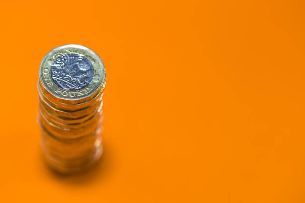 Stacked Pound Coins from above on a Bright Orange Background Copy, Negative Space With a sharp focus on the top coin, quickly dropping away, a stack of pound coins shot from above. Studio shot on a bright, modern orange background allowing negative copy space. one pound coin stock pictures, royalty-free photos & images