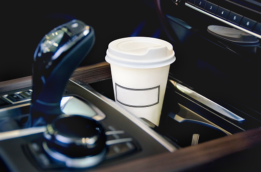 Coffee in the car salon. A single paper coffee cup inside the car cup holder. transport concept - close up.