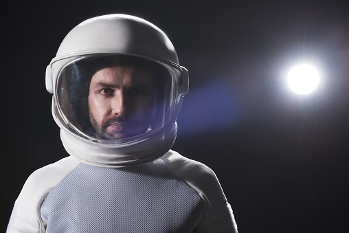 Sense of responsibility. Portrait of serious bearded astronaut wearing helmet and hyperbaric protective costume is standing and looking at camera confidently. Black background with copy space