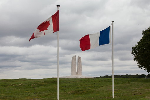 Vimy in France: Canadian National Vimy Memorial Dark clouds over the white marble monument. people can be seen. The site is dedicated to the memory of Canadian Expeditionary Force members killed during the battle of Vimy Ridge in First World War. The central columns have statues between with others at the top. the Canadian Flag and the French Flag fly in the wind