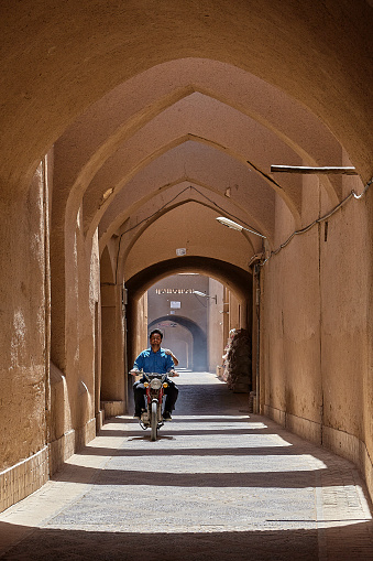 Yazd: An unknown young Iranian man is riding a moped along a narrow arched street.