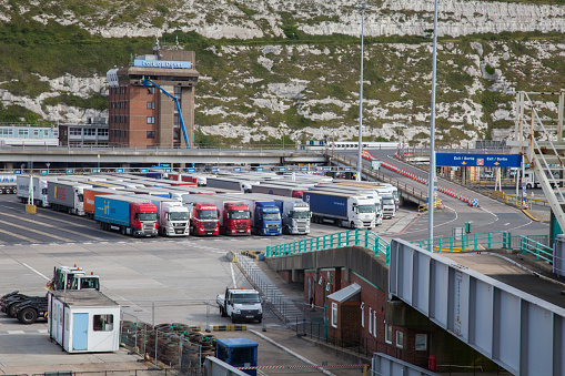 Dover Port Dock England. the white chalk of Dover Cliff's in the distance. The loading bay of terminal with lorries all ready to load on the ferry.  Cones divide the road to the right of the image. some people may be visible in the image