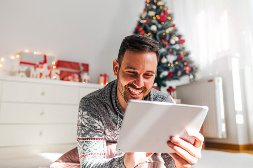 Smiling modern young man using tablet at home for Christmas
