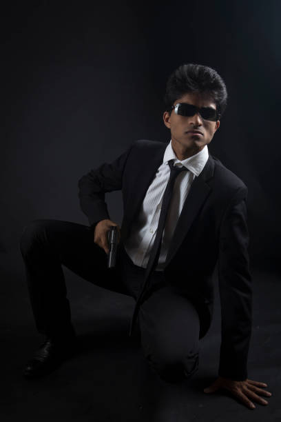 Secret agent pose Portrait of an asian man wearing an elegant suit, he is holding a gun against a black background. bounty hunter stock pictures, royalty-free photos & images