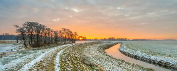 Meandering River in Frozen grassland landscape on early morning with rising sun under beautiful sky