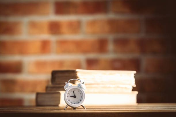 vintage alarm clock and old books on wooden table at brick wall background. Library