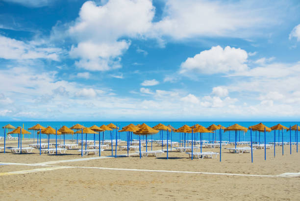 Empty perfect dreamy paradise beach with umbrellas tents made of palm leaves and white beach lounge chairs standing at the sandy bay by the blue sea and beautiful cloudy sky. Vacation holidays concept Empty perfect dreamy paradise beach with umbrellas tents made of palm leaves and white beach lounge chairs standing at the sandy bay by the blue sea and beautiful cloudy sky. Vacation holidays concept torremolinos beach stock pictures, royalty-free photos & images