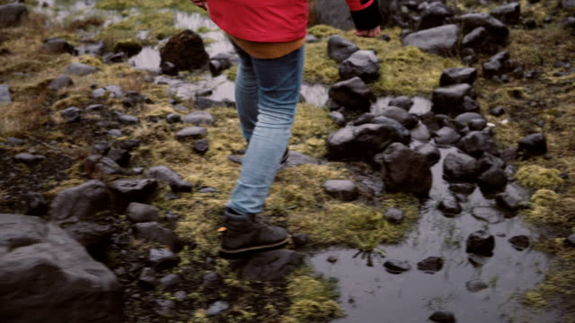 Back view of young woman hiking in rocky hills. Traveling female exploring the Iceland alone, walking through the bogs