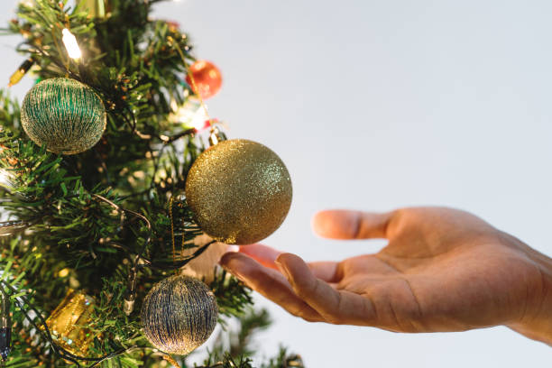 main tenant des boules de noël or étincelants sur l’arbre de noël pour décorer en vacances - christmas ball christmas ornament human hand photos et images de collection