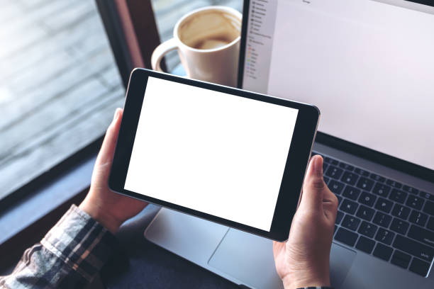 istock Mockup image of hands holding black tablet pc with white blank screen , laptop and smartphone on table in cafe 895944990