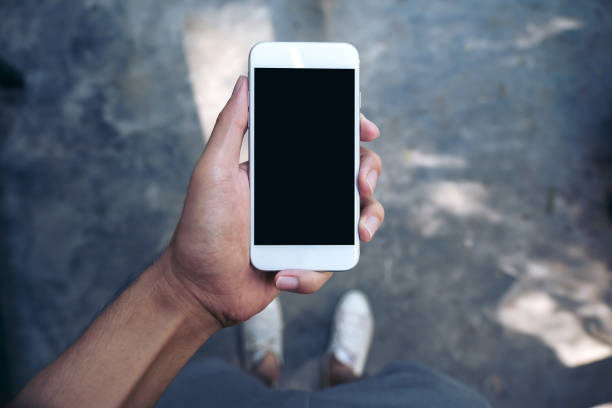 istock Mockup image of a man's hand holding white mobile phone with blank black screen while standing on concrete polishing floor 895945138