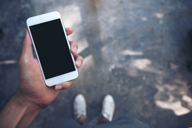 istock Mockup image of a man's hand holding white mobile phone with blank black screen while standing on concrete polishing floor 895945158