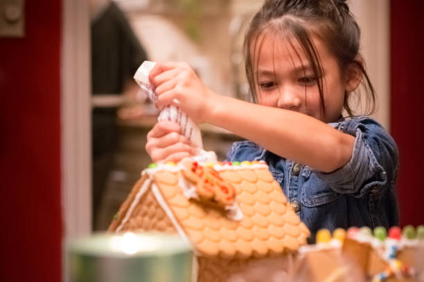 Little girl decorating Christmas gingerbread house stock photo