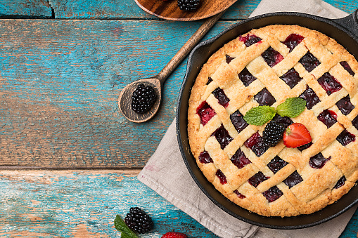 Homemade Traditional berry pie in a frying pan, sweet baked pastry food on rustic wooden table, top view