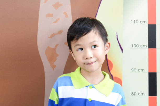 Little boy checking his height at school with measuring height scale on the wall by himself.Smiling cute asia boy measures his height. Boy growing concept
