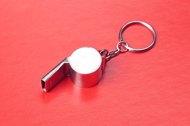 Top view of metal whistle with yellow string on dark gray background