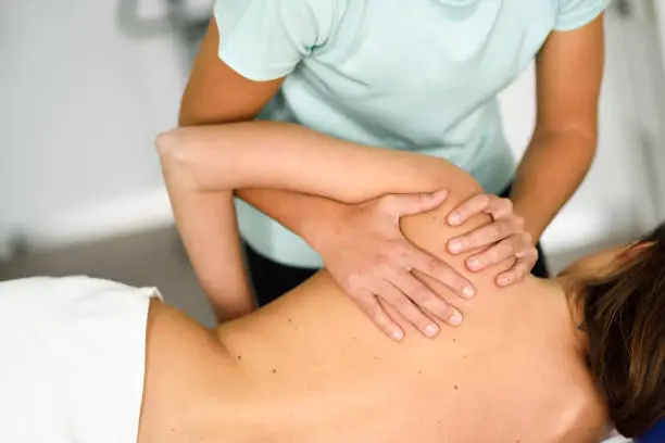 Professional female physiotherapist giving shoulder massage to brunette woman in hospital. Medical check at the shoulder in a physiotherapy center.