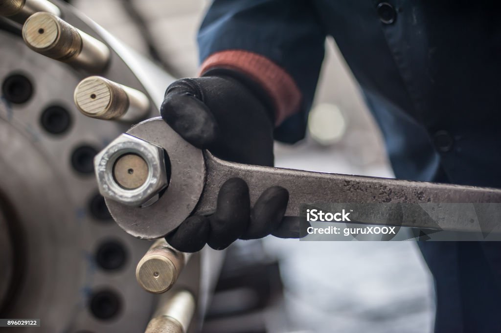 Mechanic screws big bolt with large and heavy wrench key Mechanic repairman at the factory screws big bolt with large and heavy wrench key, holding it with both hands Industry Stock Photo