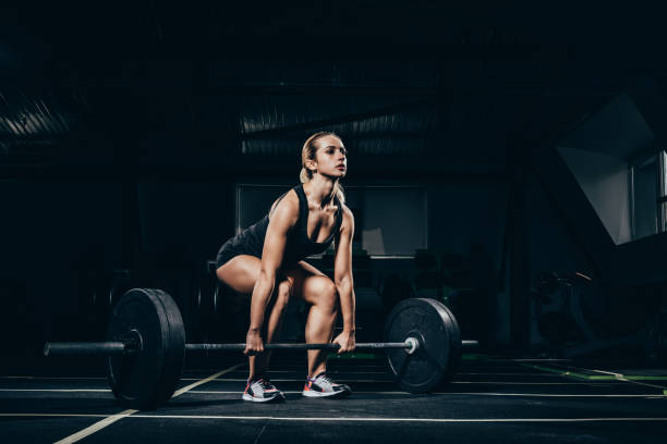sportswoman lifting barbell Young athletic sportswoman squatting while lifting a barbell with weights in gym weightlifting stock pictures, royalty-free photos & images