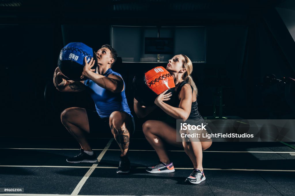 couple squatting with weighted balls Young athletic man and woman squatting with weighted balls at gym Cross Training Stock Photo