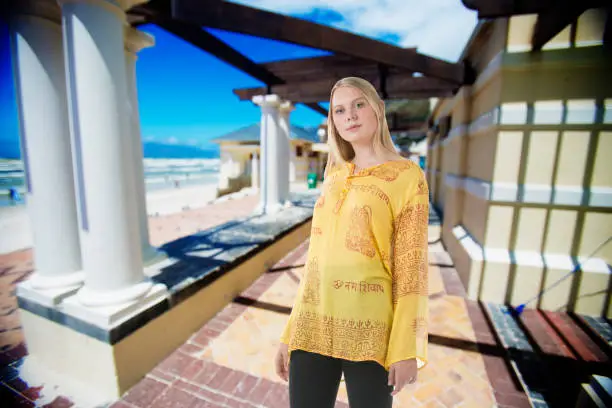 Photo of Attractive young blond woman with stylish yellow top stands near the beach at summer
