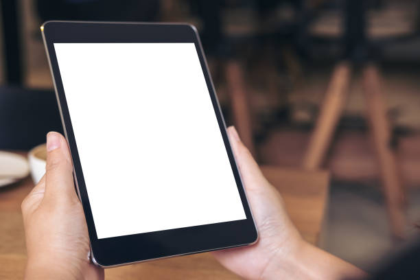 istock Mockup image of hands holding black tablet pc with blank white screen with coffee cup on wooden table in cafe 896065626