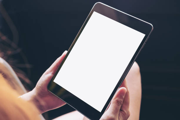 Mockup image of woman's hands holding black tablet pc with blank white screen on thigh with concrete floor background in modern cafe