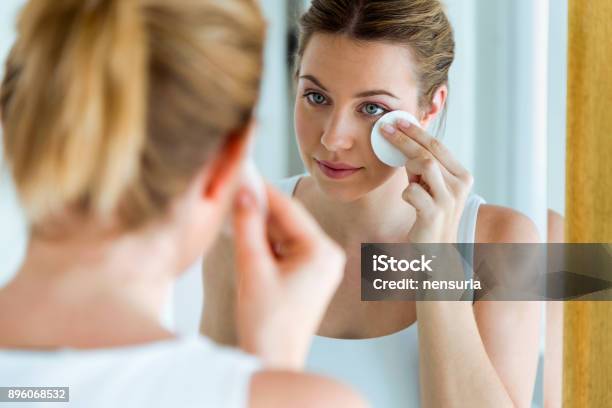 Hermosa Joven Está Limpiando Su Cara Mientras Se Mira En El Espejo En El Baño Foto de stock y más banco de imágenes de Quitarse el maquillaje