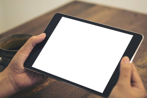 istock Mockup image of hands holding black tablet pc with blank white screen and coffee cup on wooden table background in cafe 896068776