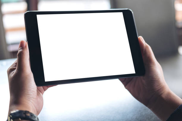 istock Mockup image of hands holding black tablet pc with white blank screen on wooden table background in cafe 896068828
