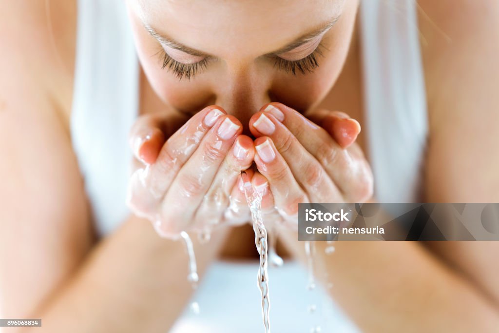 Bella giovane donna che si lava il viso spruzzando acqua in un bagno di casa. - Foto stock royalty-free di Lavarsi il viso