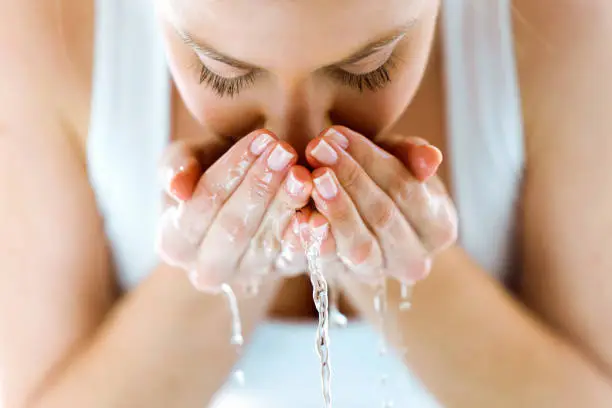 Photo of Beautiful young woman washing her face splashing water in a home bathroom.