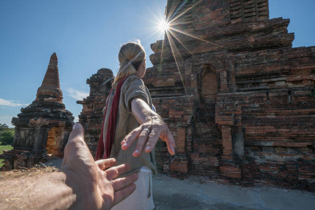 Follow me concept- Caucasian young woman leading boyfriend to the Bagan archeological zone at sunrise, temples pagodas and monastery coming out from the lush greenery. People travel concept.