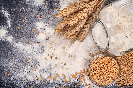 A glass jar with flour and grain sprinkled on a black background