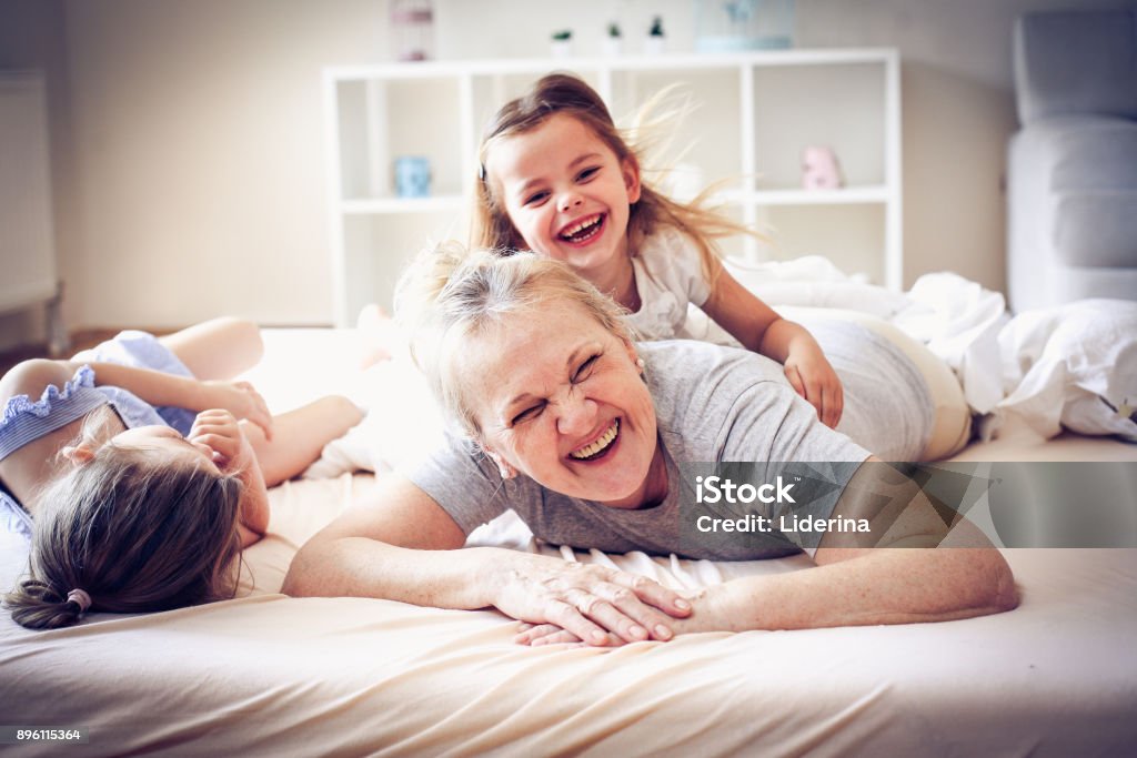 Playing in bed. Grandmother enjoying in bed with her little granddaughters. Nanny Stock Photo