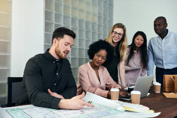 istock Group of designers discussing blueprints at an office table 896115776