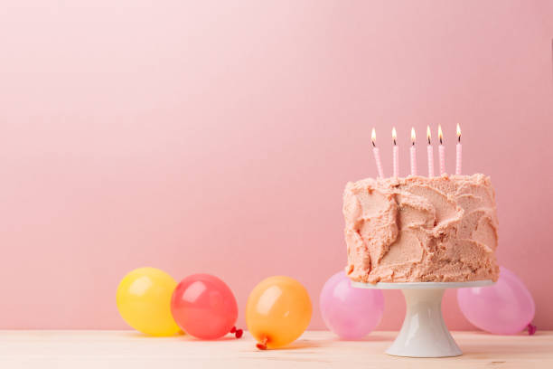istock Delicious cake with pink icing on cake stand decorated with burning candles on pink background. 896148498