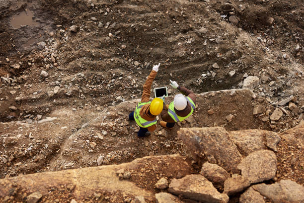 Construction Workers Inspecting Site Top view shot of two industrial workers wearing reflective jackets standing on mining worksite outdoors using digital tablet, copy space precious metals stock pictures, royalty-free photos & images