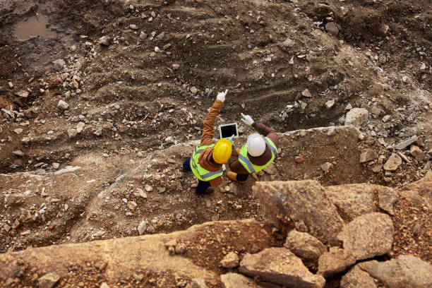 Construction Workers Inspecting Site Top view shot of two industrial  workers wearing reflective jackets standing on mining worksite outdoors using digital tablet, copy space open pit mine stock pictures, royalty-free photos & images