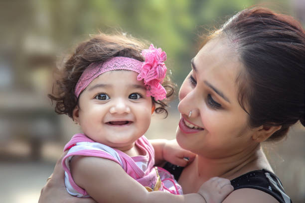 행복 한 인도 엄마와 딸이 공원에서 녹색 배경 위에 미소. 선택적 초점, 필드의 얕은 깊이입니다. - baby toddler young women outdoors 뉴스 사진 이미지