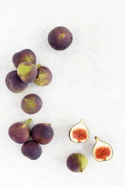 Arrangement of fresh whole and cut figs and on a white marbled background with lots of copy space. Top view.