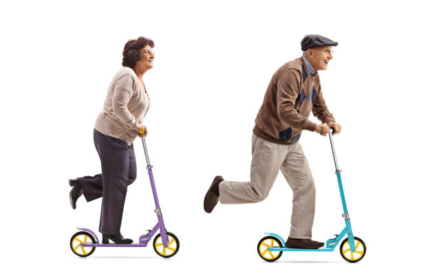 Full length profile shot of an elderly woman and an elderly man riding scooters isolated on white background