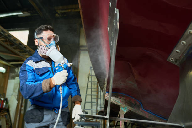 Worker Painting Boats in Yacht Workshop Low angle portrait of unrecognizable worker wearing protective mask painting boat using paint sprayer in yacht workshop, copy space motorboat maintenance stock pictures, royalty-free photos & images