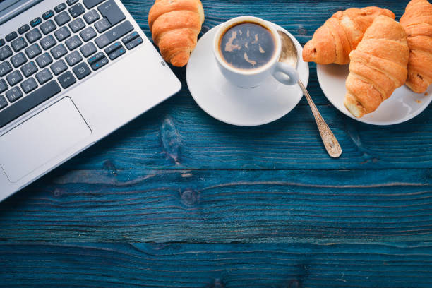 Business breakfast, coffee and croissants, on a wooden surface. Top view. Free space for text.