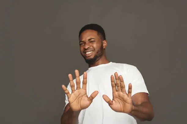 Black man expressing disgust on face, grimacing on white studio background. Negative emotions