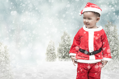 Cute santa kid with motion blur falling snow on winter background and copy space for add your text