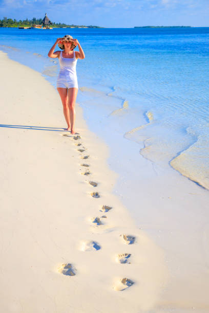 Woman with hat and footsteps walks on the sandy beach by the sea Woman with hat and footsteps walks on the sandy beach by the sea meeru island stock pictures, royalty-free photos & images