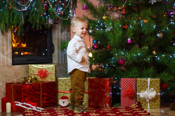 かわいい金髪の暖炉とクリスマス ツリーの下のプレゼントの近くの小さな男の子 - gift little boys people blond hair ストックフォトと画像