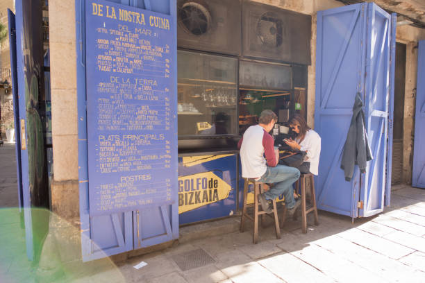 Barcelona, Spain, Oct. 14, 2017: Lens flare over a couple hanging out at a restaurant with a street side bar area in the Gothic Quarter. Such sidewalk dining areas are common in the neighborhood.